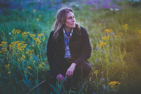 Melissa Carper kneeling in a field of wildflowers at dusk