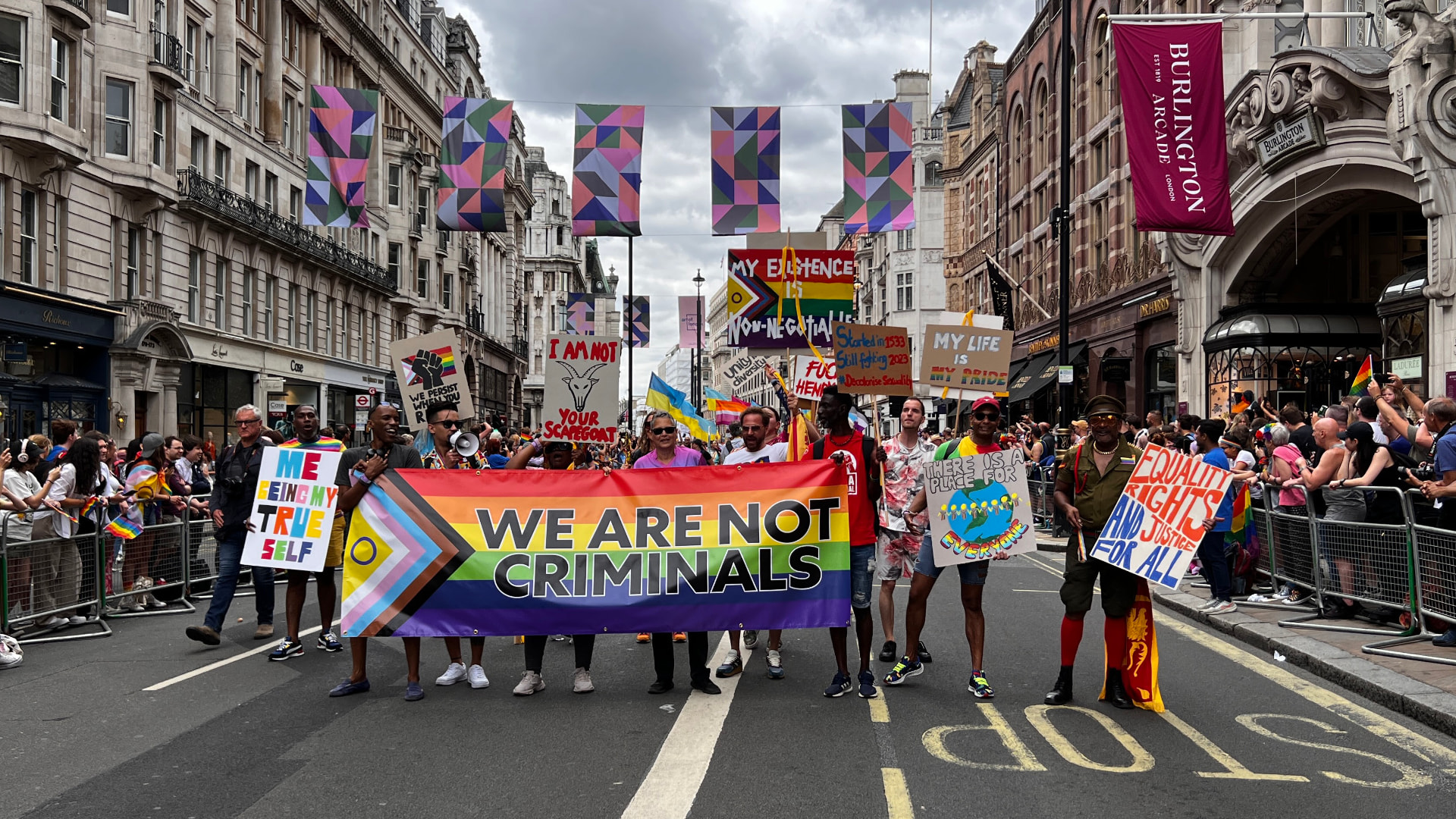 Activists marching at London Pride behind a rainbow banner reading 'We Are Not Criminals', from Out Laws (credit: Emily N. Kanga)