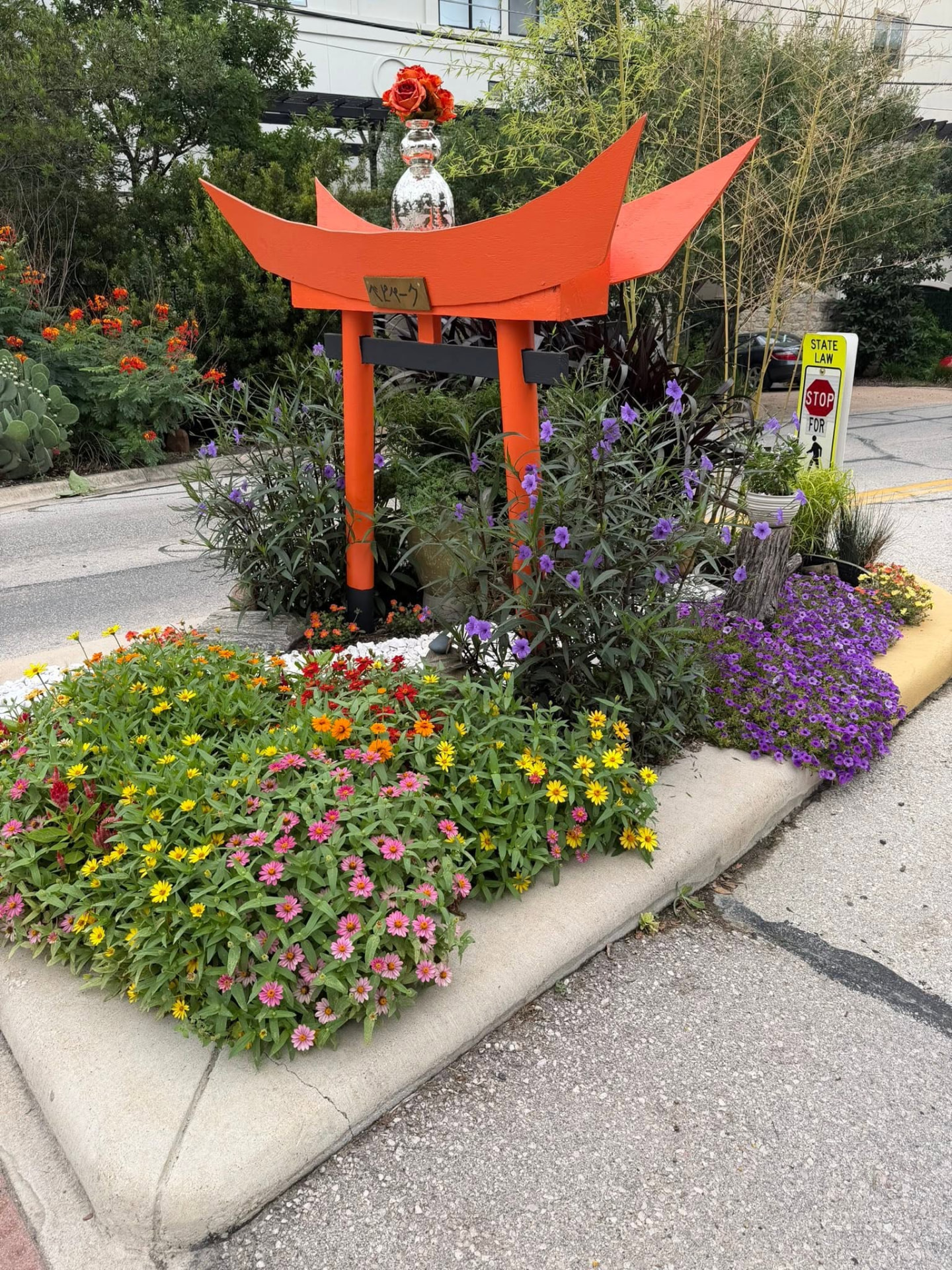 Orange torii gate sculpture surrounded by zinnias and petunias at BEPI Park