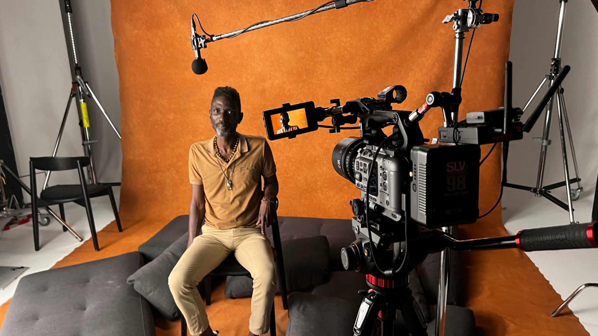 Behind the scenes in the UK: Friedel Dausab seated for an interview in front of an orange backdrop with camera and boom mic (credit: James Lewis)