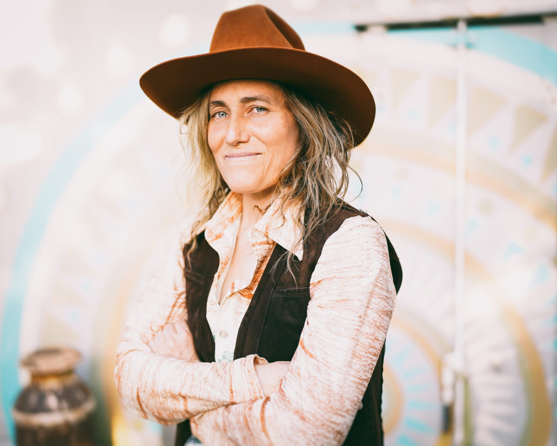 Melissa Carper in a brown wide-brim hat, arms crossed, in front of a painted mural
