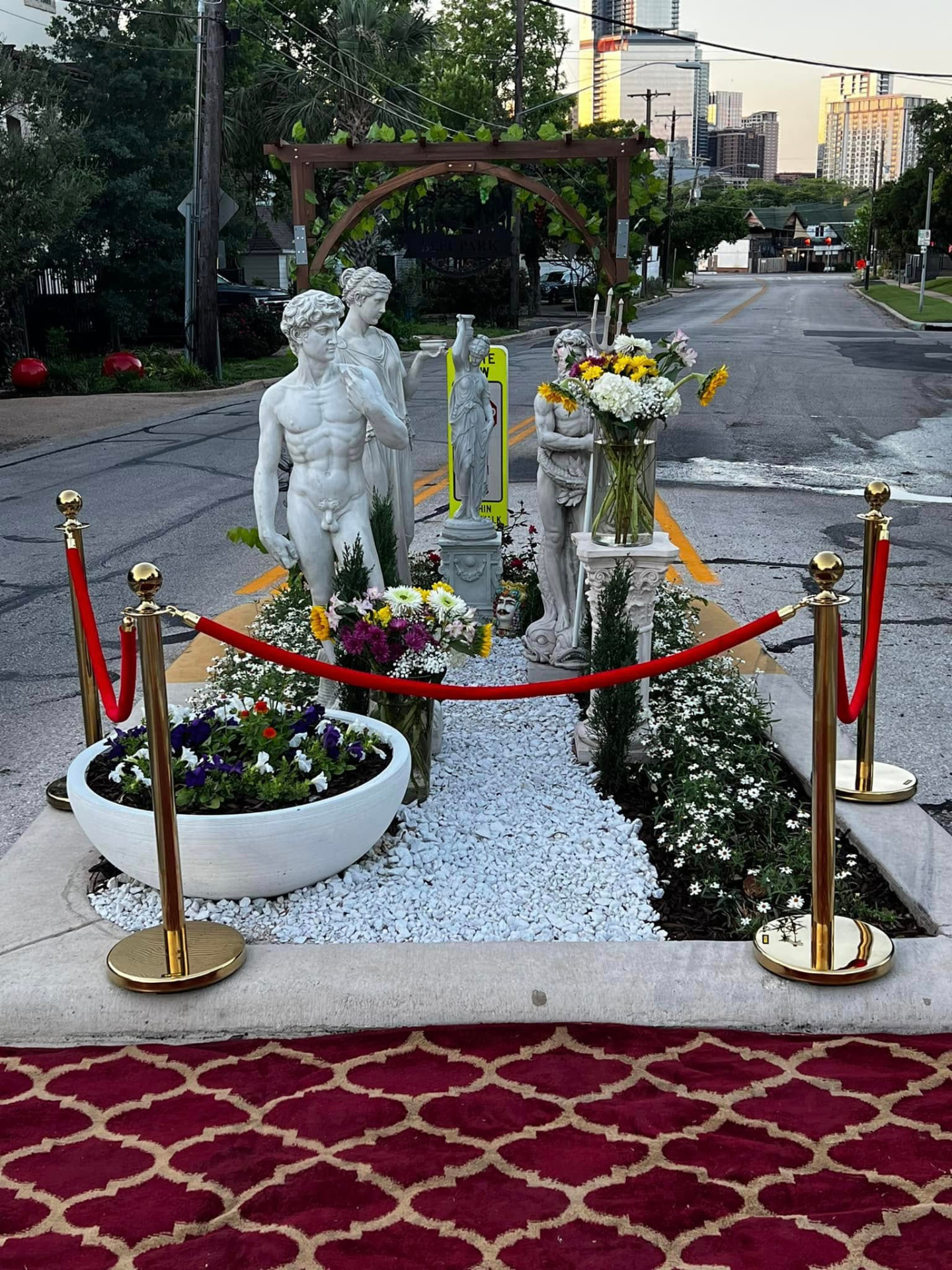 Red carpet and velvet ropes laid at BEPI Park, Austin's tiniest park, with classical statues and downtown skyline behind