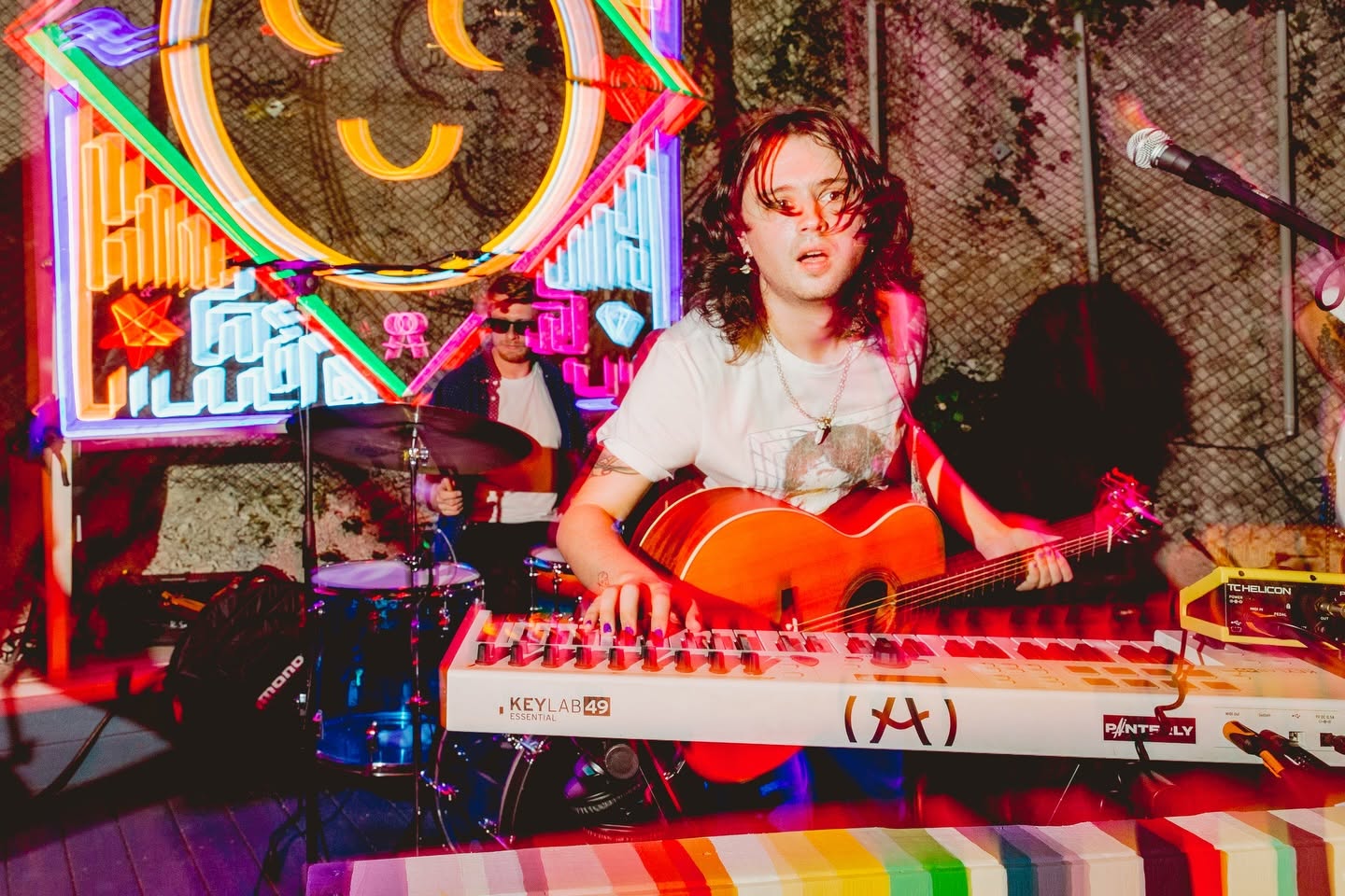 Painterly's Jonathan Barrett playing guitar and keys in front of a neon smiley sign