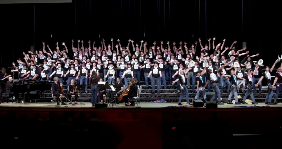 The full Austin Gay Men's Chorus on stage with arms raised at the GALA Choruses Festival