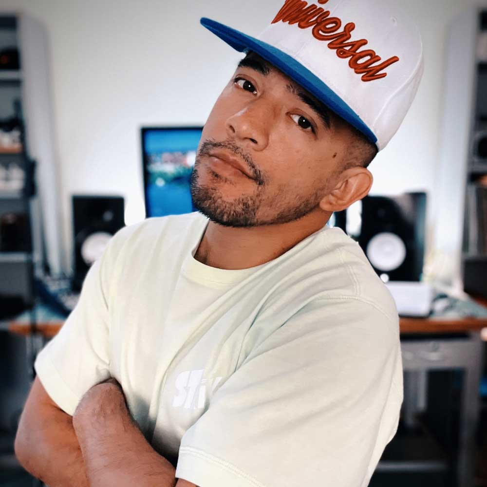 Gabriel 'Bboy Wicket' Dionisio in a Universoul cap, arms crossed, in his home studio